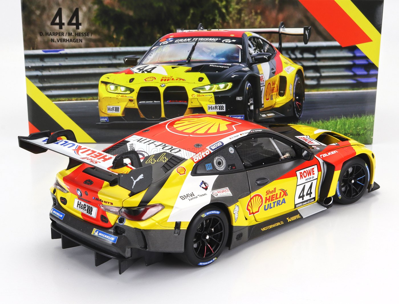 Modèle réduit détaillé de la voiture de course BMW M4 GT3 aux couleurs Shell Helix Ultra avec décalcomanies de course, présenté avec une image d'arrière-plan, disponible sur Vroomi.