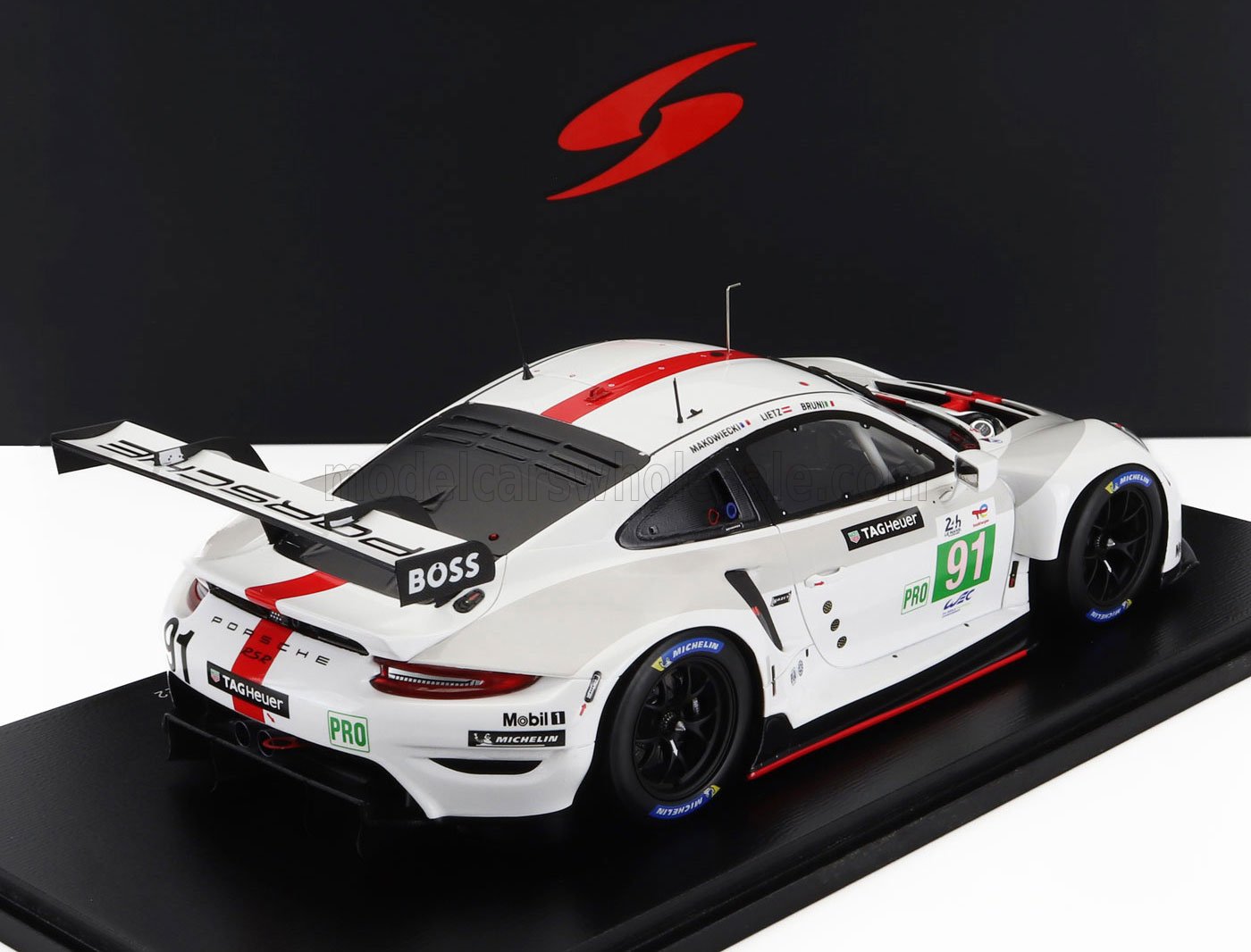 White Porsche 911 RSR race car model with red stripe and number 91, displayed on black stand, available via Vroomi
