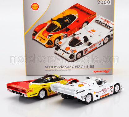 Deux voitures de course Porsche 962 C Shell aux couleurs rouge-jaune et blanc avec des décalcomanies détaillées, présentées dans leur emballage ; disponibles sur Vroomi.