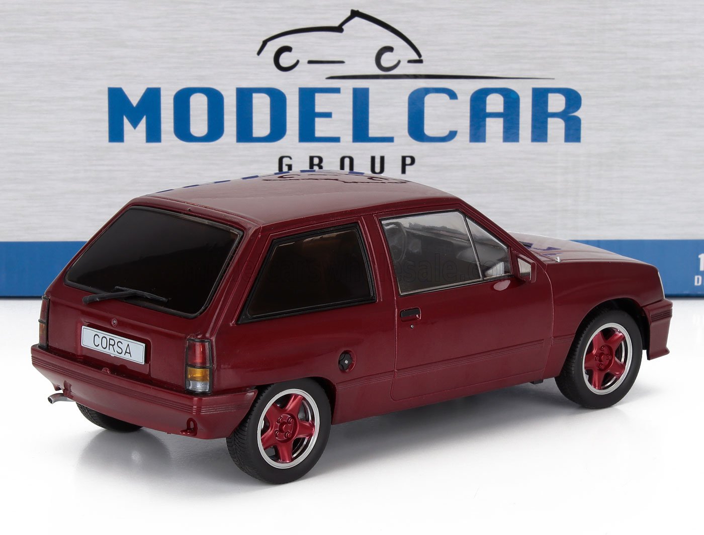 Modèle réduit de voiture Red Corsa à l'échelle 1/43 avec vitres teintées, présenté sur un socle blanc avec un fond Model Car Group, disponible chez Vroomi.