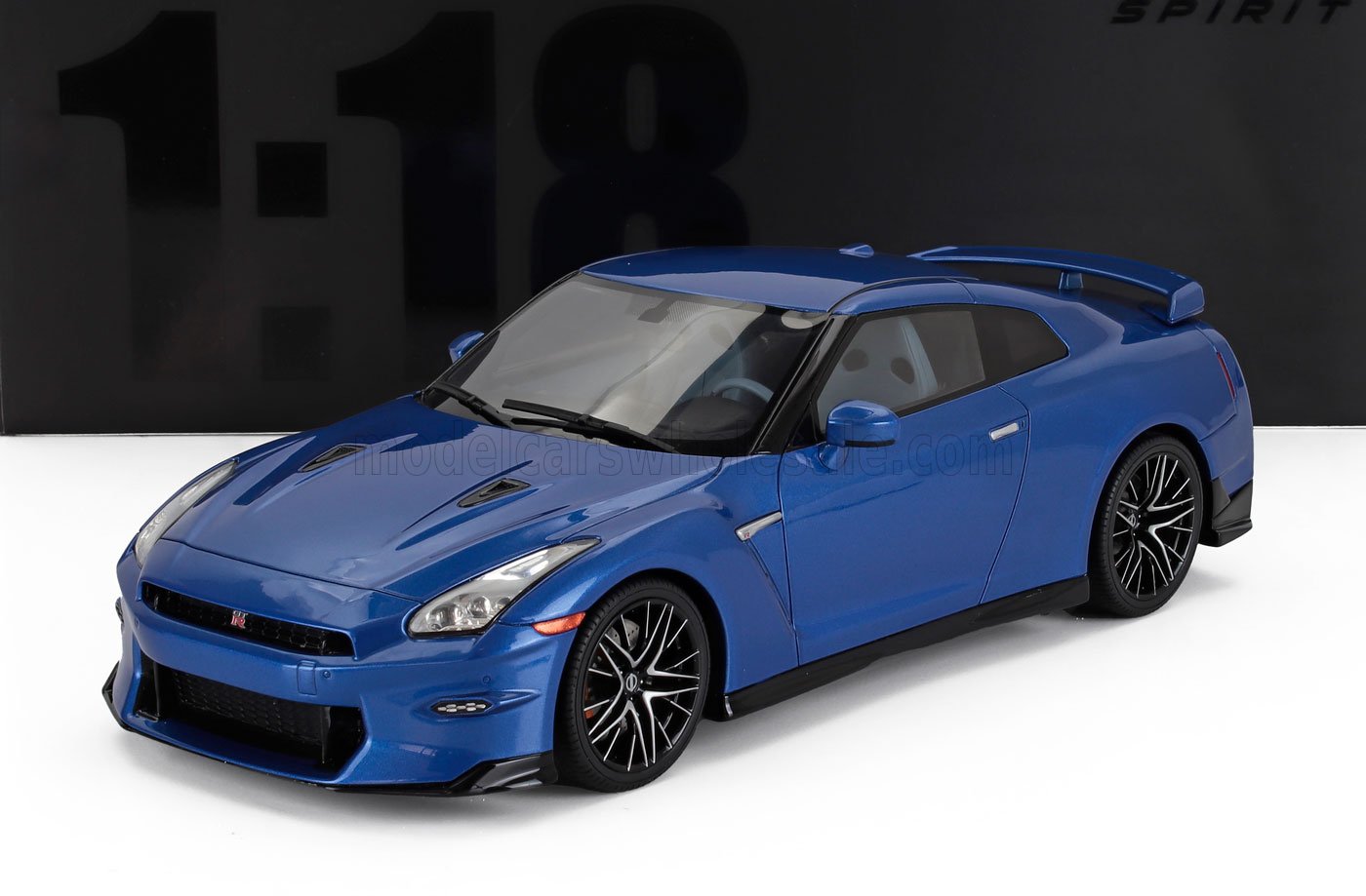Modèle réduit de voiture Nissan GT-R R35 bleu avec jantes en alliage noires, présenté sur une surface blanche avec un fond noir, disponible chez Vroomi.