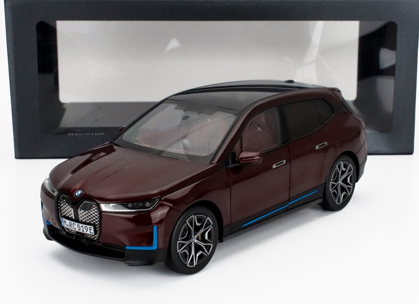 Modèle réduit BMW X7 rouge foncé avec toit noir et accents bleus, présenté dans son coffret, disponible sur Vroomi.