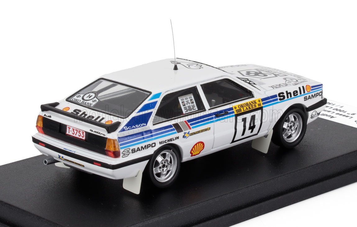 Voiture de rallye Audi Quattro blanche avec autocollants Shell et Sampo, numéro 14, présentée sur un socle noir, proposée par Vroomi.