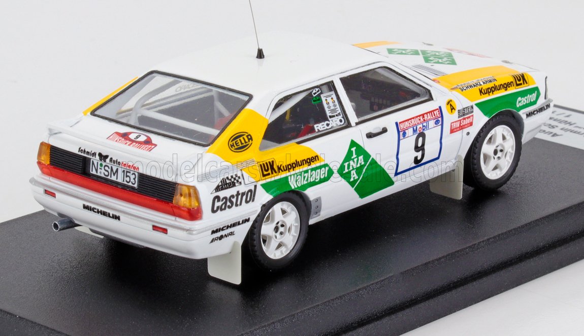 Modèle réduit de voiture de rallye Audi blanche avec décalcomanies vertes et jaunes, numéro 9 et logos des sponsors, présenté sur un socle noir, disponible sur Vroomi.