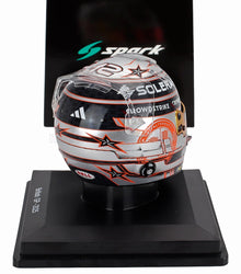 Casque de course miniature à l'échelle 1/5 avec motif étoilé argenté, noir et orange et logos des sponsors sur socle d'exposition, disponible chez Vroomi.