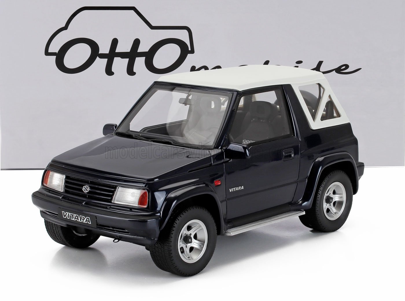 Maquette réduite d'une Suzuki Vitara noire avec toit blanc, exposée devant un décor mobile Otto, sur Vroomi.