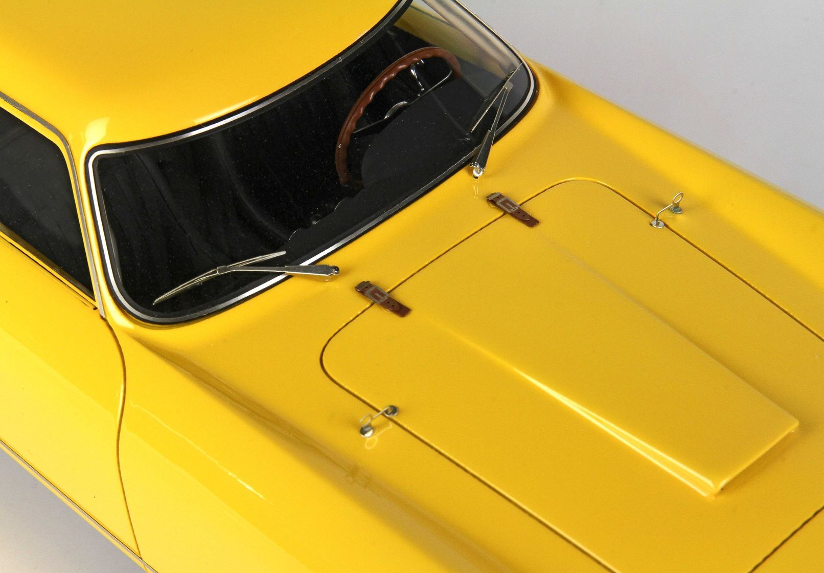 Gros plan sur le capot et le pare-brise jaunes d'une voiture vintage avec un volant marron, disponible via Vroomi.