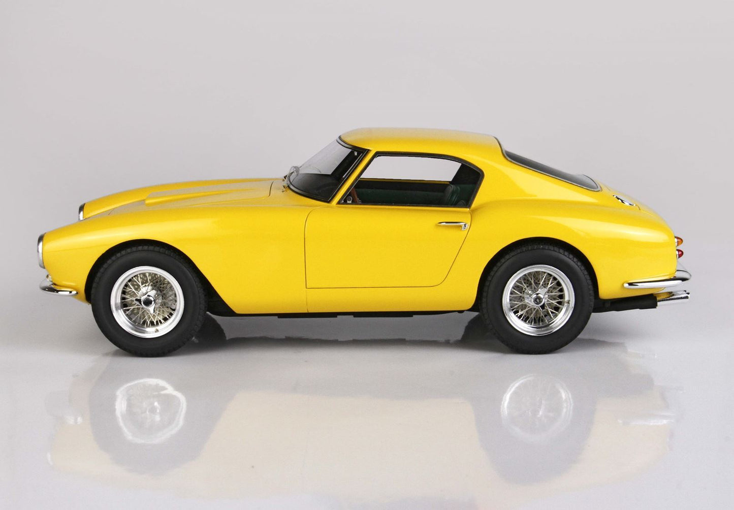 Modèle réduit de voiture de sport vintage jaune avec jantes à rayons, carrosserie coupé élégante, présenté sur une surface réfléchissante, proposé sur Vroomi.