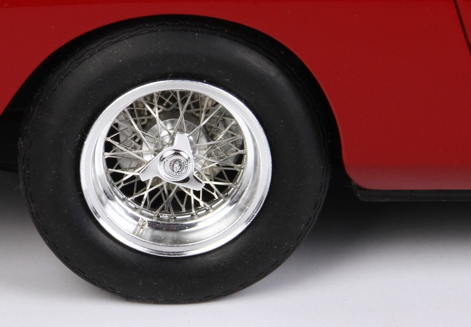 Gros plan sur une roue à rayons argentés avec moyeu triangulaire amovible sur une voiture classique rouge, disponible sur Vroomi.