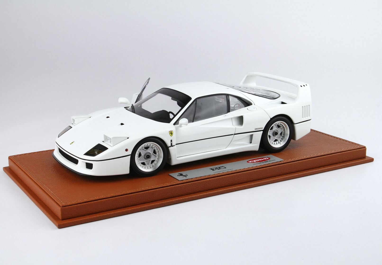 Modèle réduit de Ferrari F40 blanche avec porte ouverte, présenté sur un socle en cuir marron, disponible sur la plateforme Vroomi.