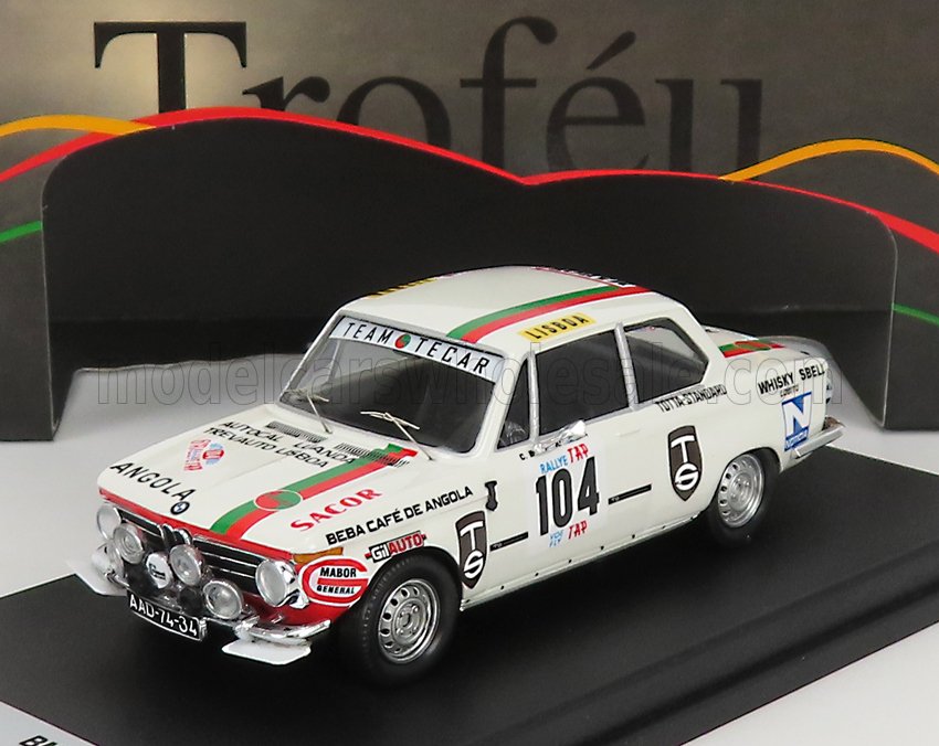 Modellino dettagliato di un'auto da rally classica bianca con strisce rosse e verdi, numero 104 e loghi degli sponsor, esposto su un piedistallo, disponibile su Vroomi.