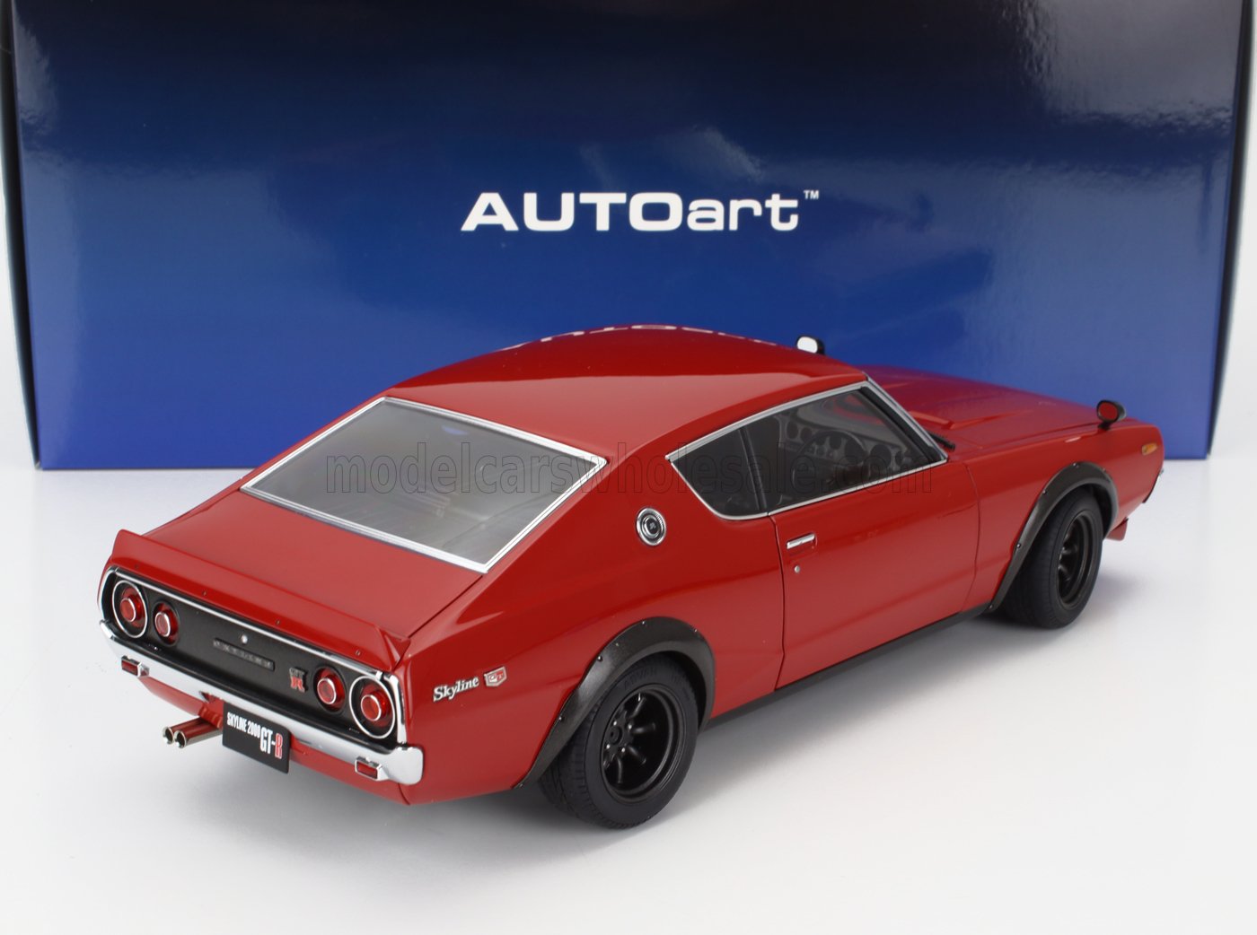 Modellino in scala della Nissan Skyline 2000 GT-R rossa di AUTOart con ruote nere, mostrato su una superficie bianca, disponibile sulla piattaforma Vroomi.