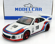 Modellino di auto da corsa sportiva in scala 1/18, bianco con strisce rosse e blu, numero 118 e cerchi rossi, esposto davanti alla scatola Modelcar Group, disponibile da Vroomi.