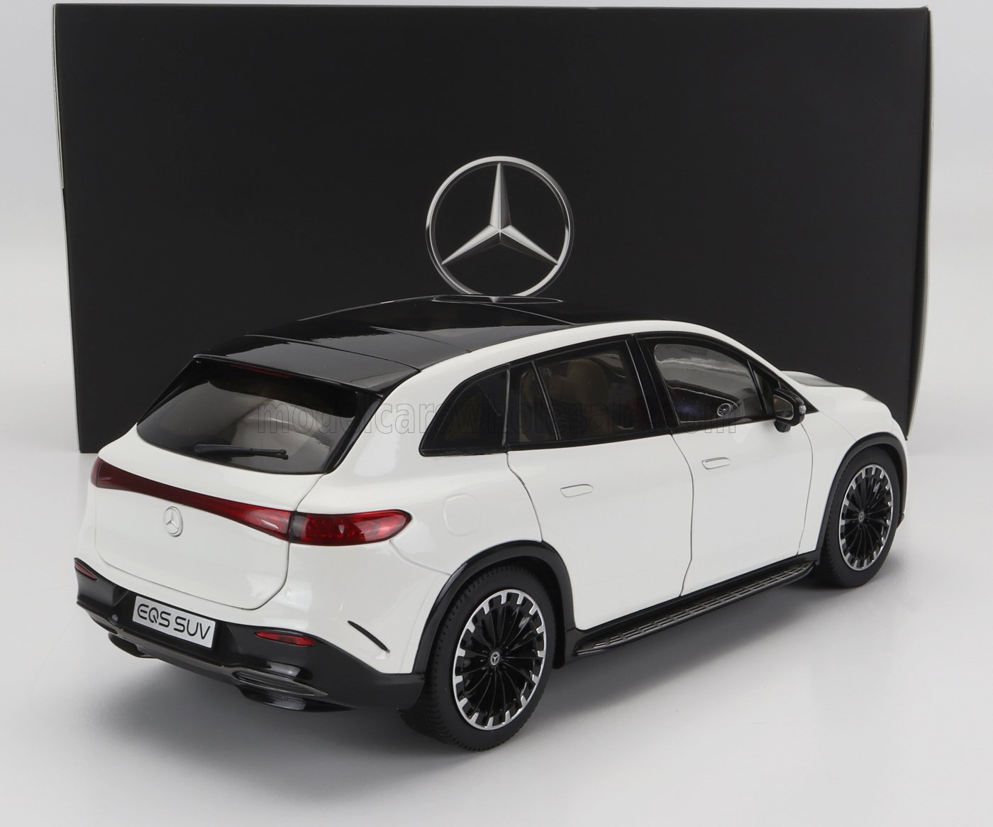 Modello SUV Mercedes EQS bianco con tetto nero e ruote dettagliate, con grande logo Mercedes sullo sfondo, disponibile su Vroomi.