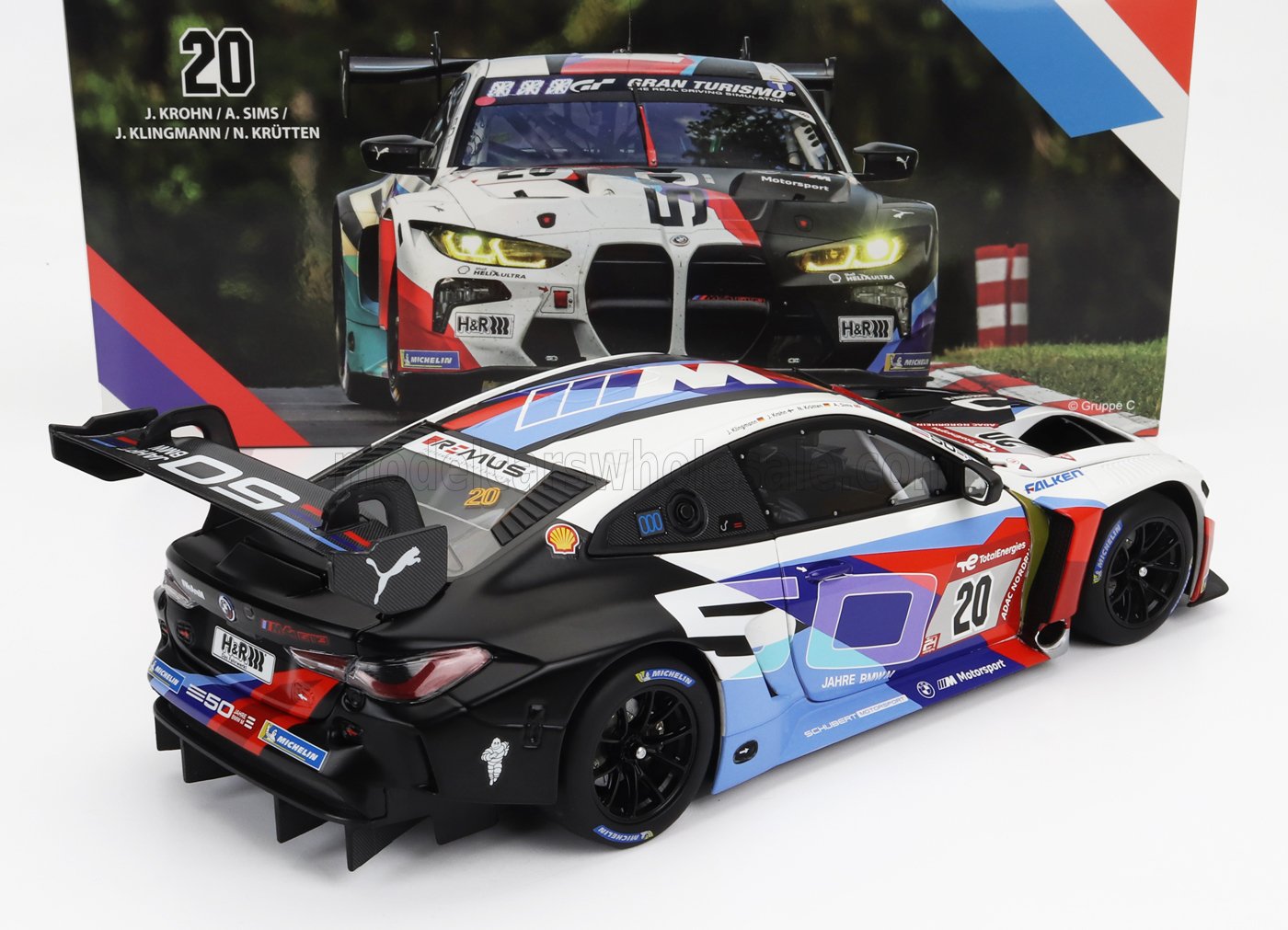 Modellino in scala della BMW M4 GT3 da corsa con livrea 50 Jahre, esposto con sfondo promozionale, disponibile su Vroomi.
