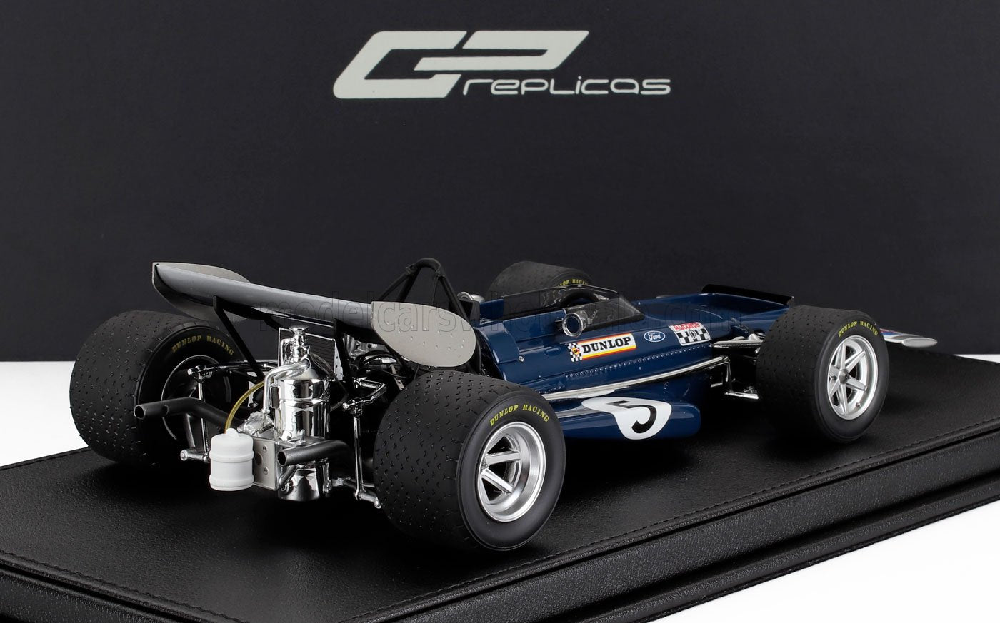 Modellino vintage blu di un'auto da corsa di Formula 1 con pneumatici Dunlop su supporto nero, disponibile tramite Vroomi.