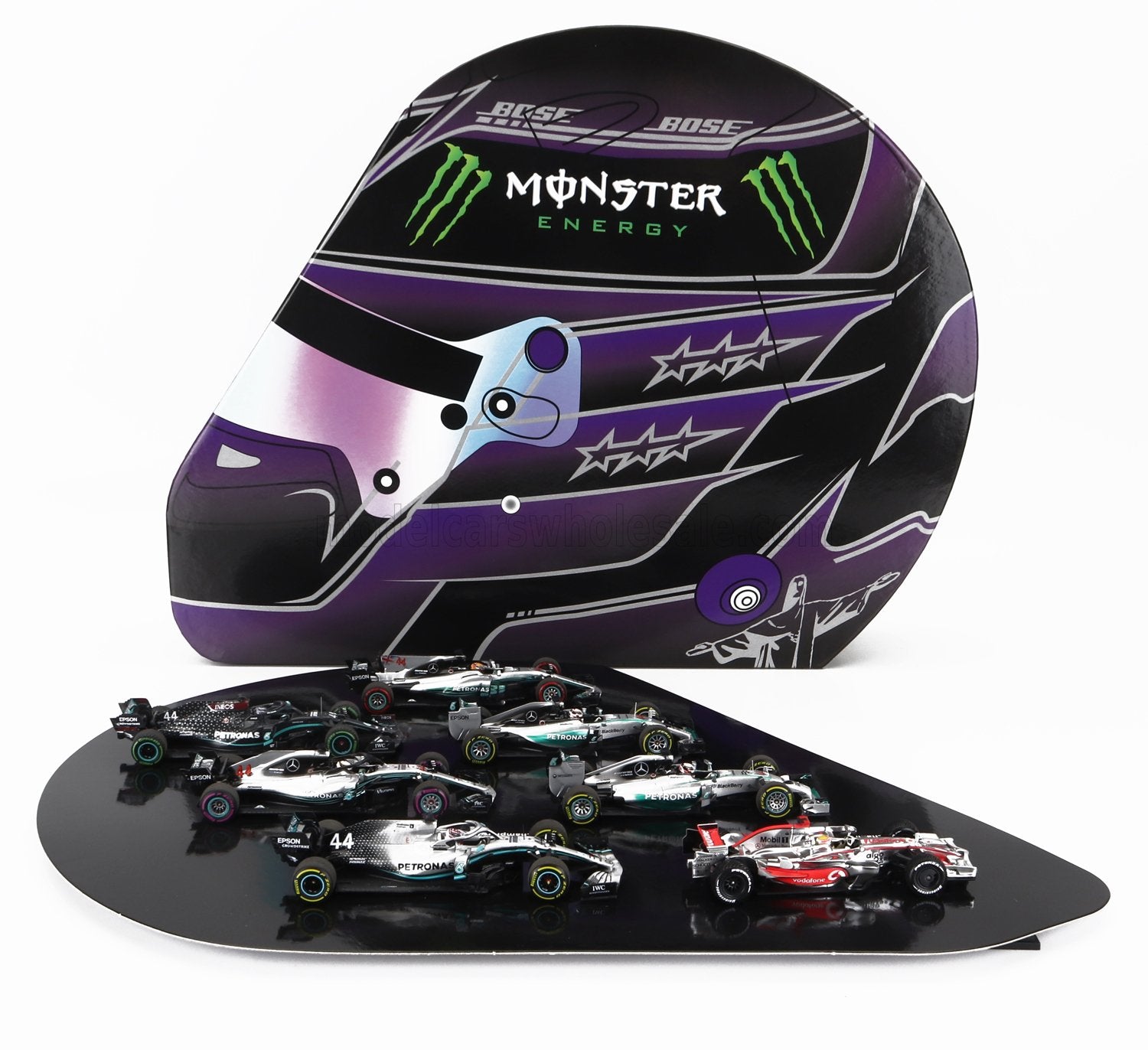Modellini da collezione di auto di F1 su base nera con un casco da corsa Monster Energy viola sullo sfondo, disponibili su Vroomi.
