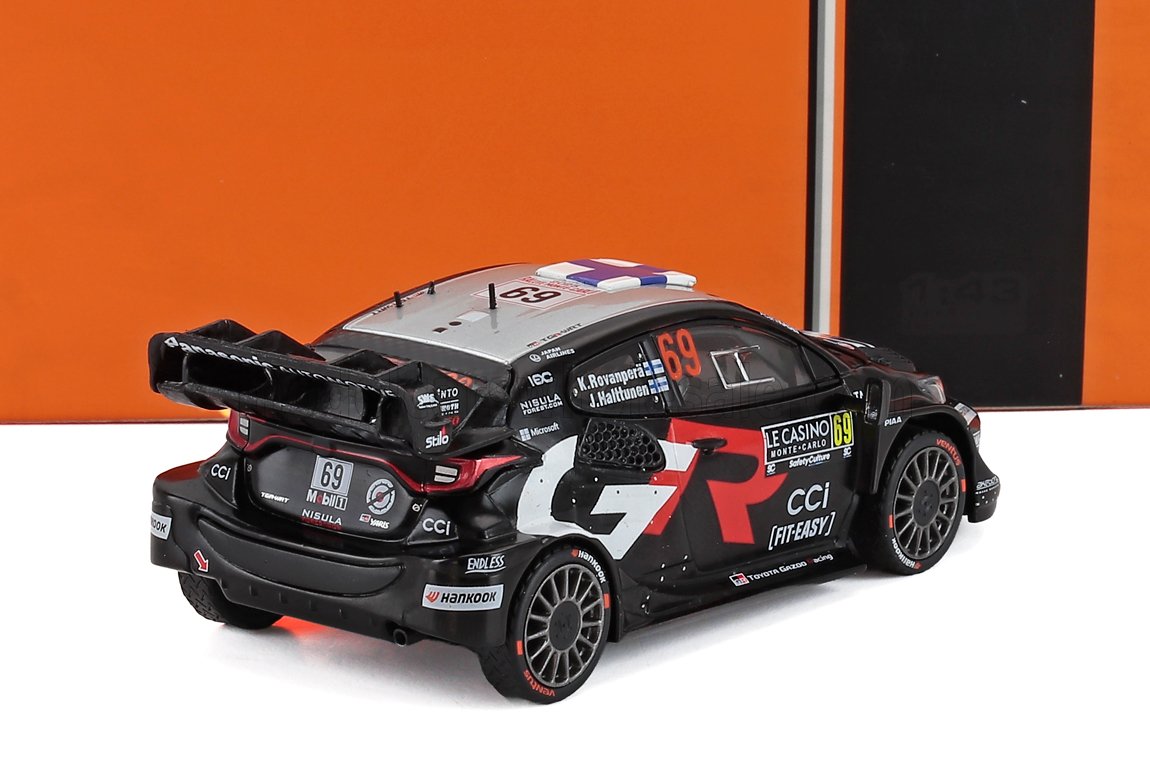 Black and gray rally car model with number 69 and sponsor decals, shown on white and orange backdrop, available on Vroomi