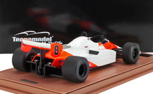 Modellino in scala di un'auto da corsa vintage di Formula 1 bianca e arancione con il numero 8, su un tappetino marrone, venduto da Vroomi.