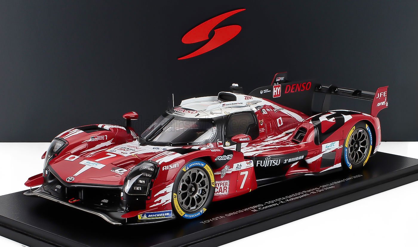 Red and white Toyota GR010 Hybrid race car model with racing decals, displayed on a stand, available on Vroomi