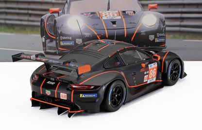 Modellino di auto da corsa Porsche 911 RSR nera e arancione con il numero 86, decorato con adesivi da gara, mostrato su uno sfondo che raffigura una pista da corsa, disponibile sulla piattaforma Vroomi.