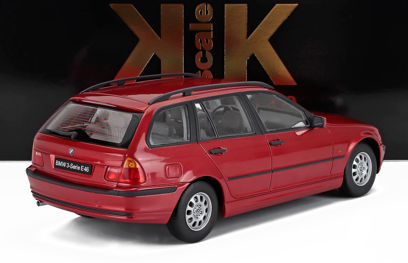 Modellino di auto BMW Serie 3 E46 station wagon rossa su superficie bianca con sfondo scuro, disponibile su Vroomi