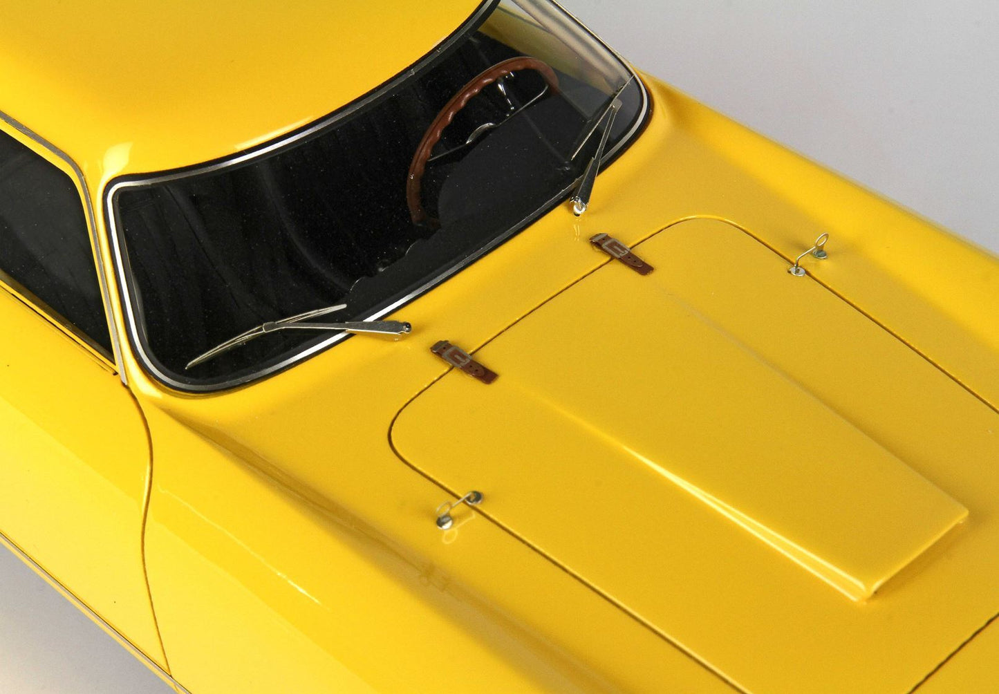 Primo piano del cofano e del parabrezza di un'auto d'epoca gialla con volante marrone, disponibile tramite Vroomi.