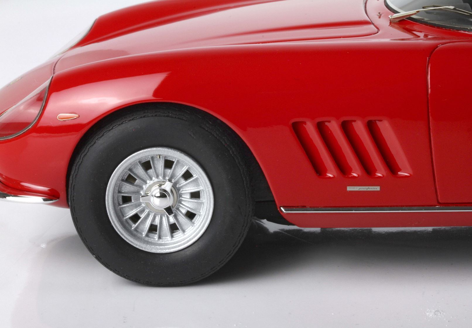 Primo piano della ruota anteriore e delle prese d'aria laterali di un'auto d'epoca rossa, con i classici cerchi in lega, disponibile su Vroomi.