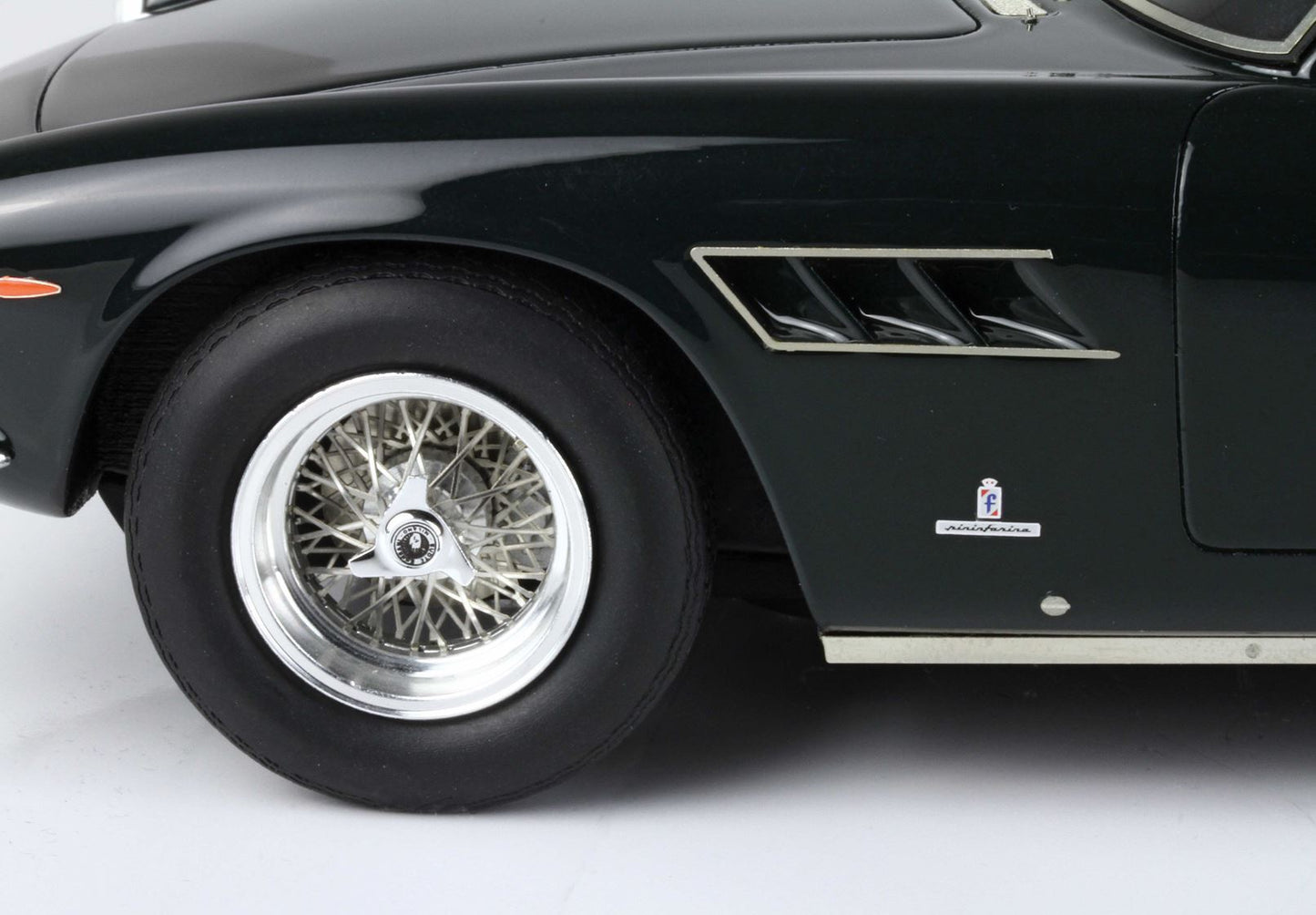 Primo piano della ruota anteriore di un'auto nera classica con raggi in filo metallico, stemma Pininfarina, disponibile su Vroomi.