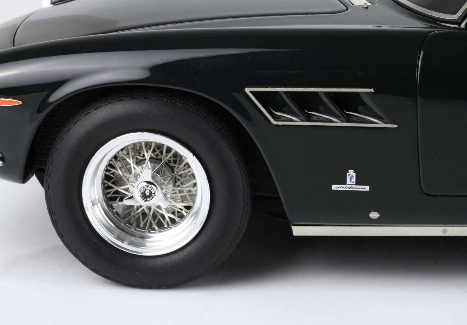 Primo piano della ruota anteriore di un'auto nera classica con raggi in filo metallico, stemma Pininfarina, disponibile su Vroomi.