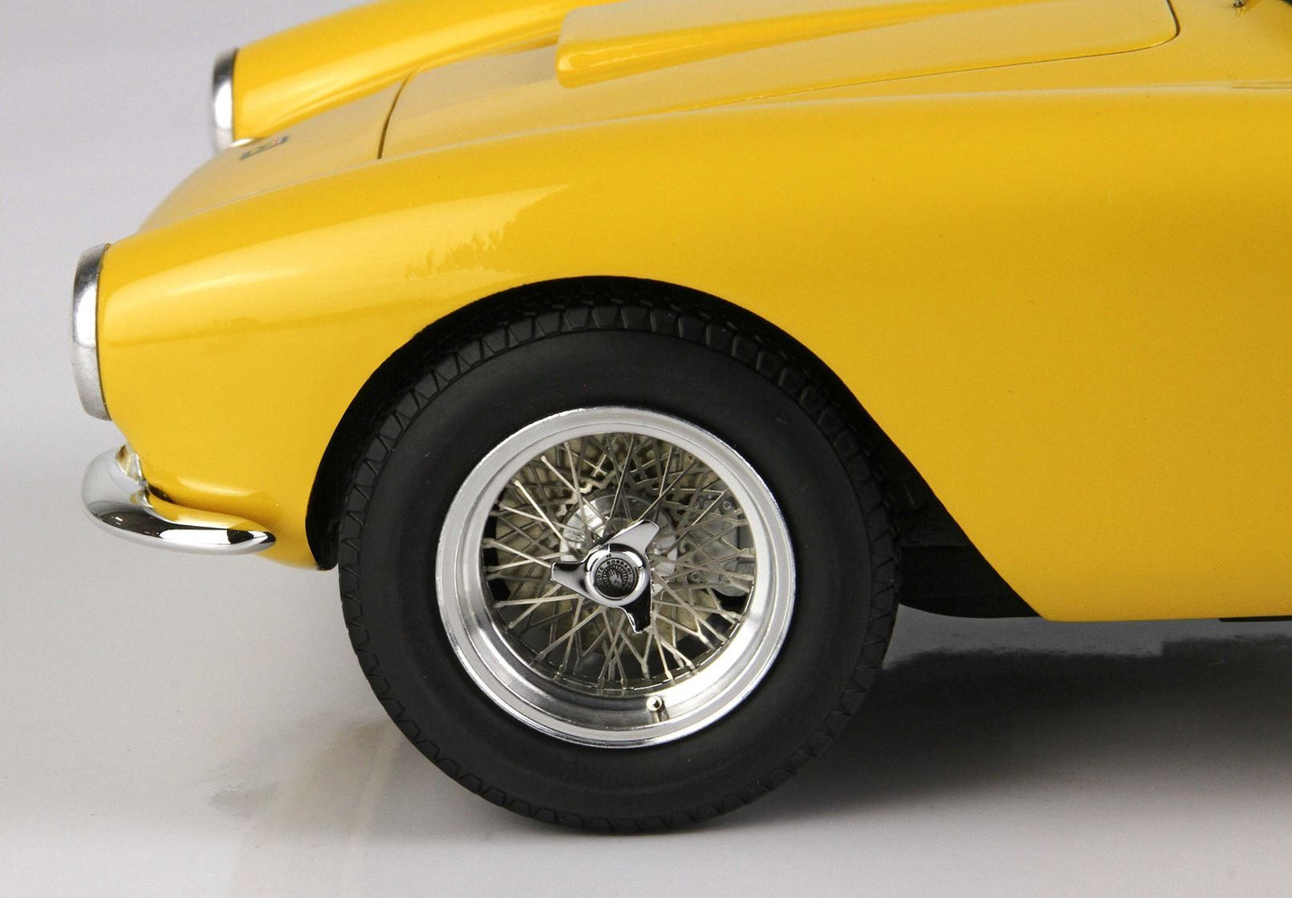 Primo piano della ruota anteriore di un'auto vintage gialla con raggi in filo metallico e coprimozzo cromato, in vendita su Vroomi.