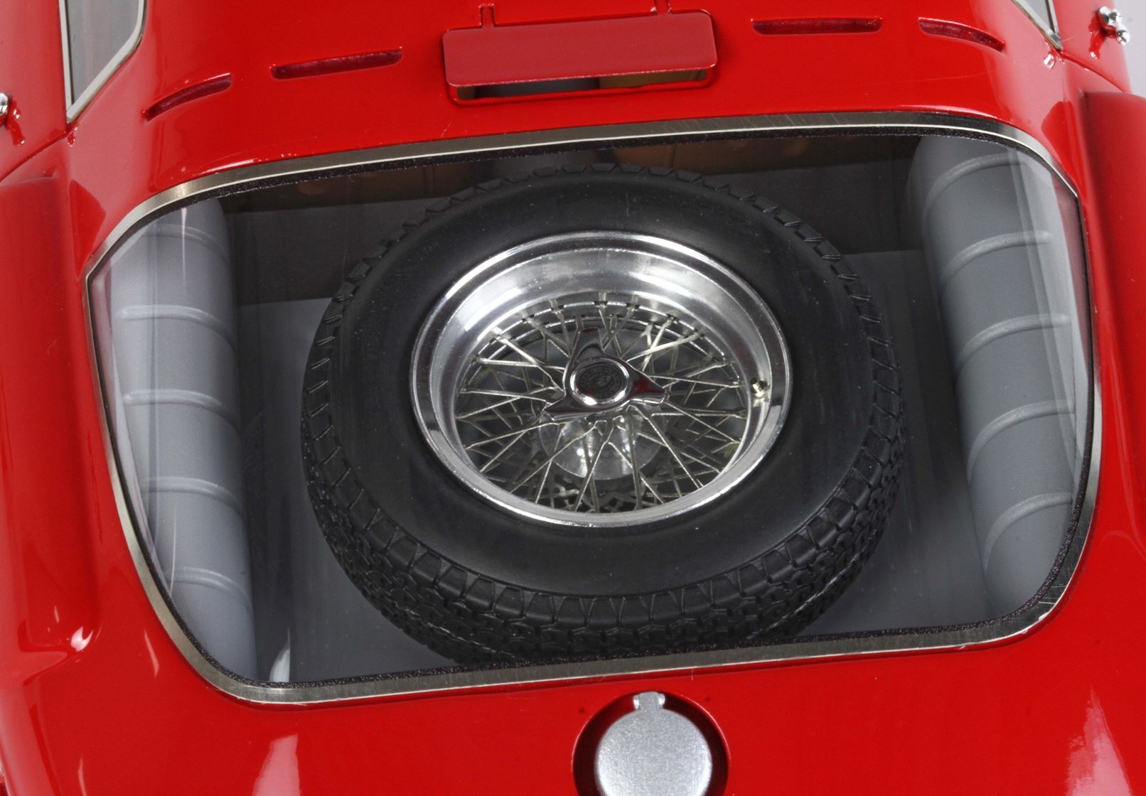Spare tire with chrome wire spoke rim in the rear compartment of a red classic car, available on Vroomi