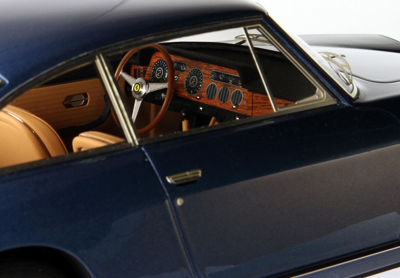 Primo piano degli interni di una classica Ferrari blu scuro in miniatura con cruscotto in legno e sedili color cuoio, ora disponibile su Vroomi.