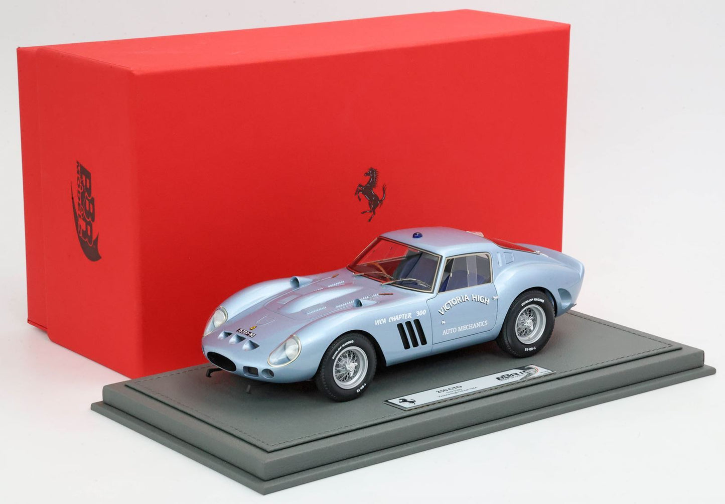 Modellino di Ferrari 250 GTO azzurro con adesivi Victoria High Auto Mechanics, esposto su un supporto grigio con scatola Ferrari rossa, disponibile su Vroomi.