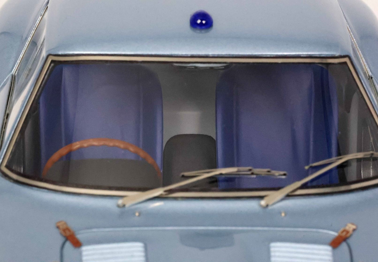 Primo piano dell'interno di un'auto d'epoca con sedili blu, volante marrone e tergicristalli, ora su Vroomi.