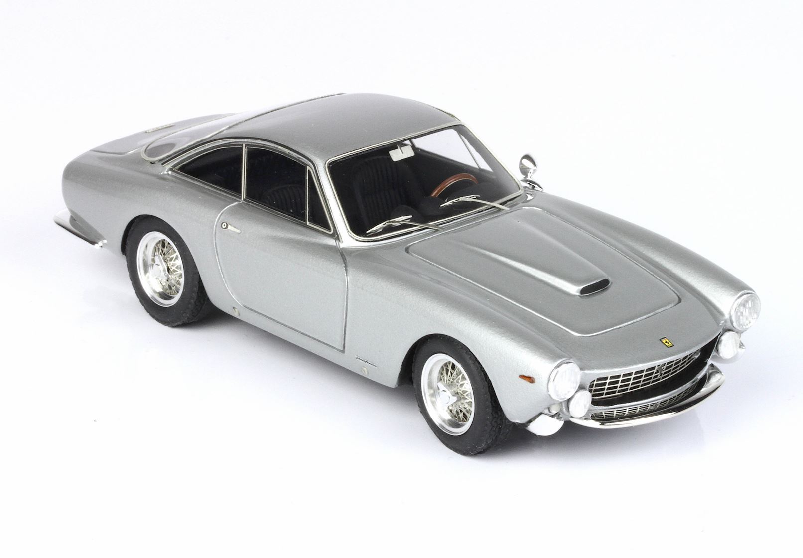 Modello classico vintage di auto sportiva argentata con cerchi a raggi, griglia dettagliata e volante in legno, disponibile su Vroomi.