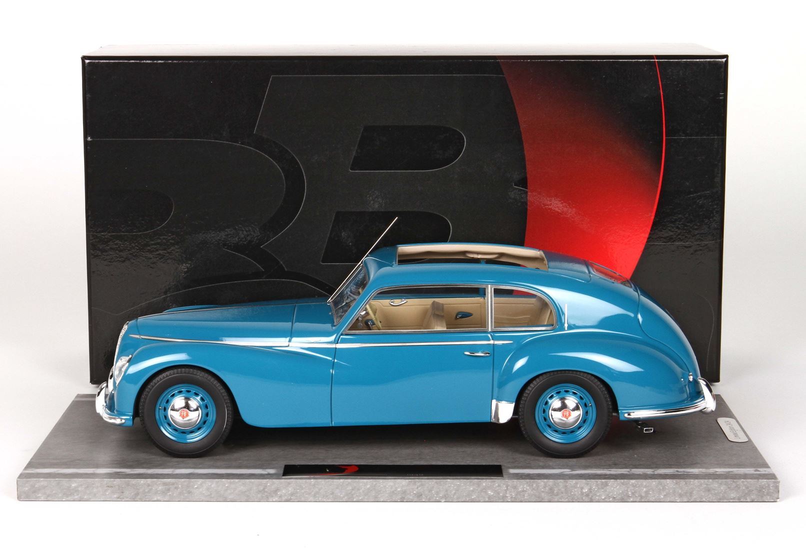 Modellino d'auto vintage blu con interni color cuoio su espositore, disponibile tramite Vroomi.