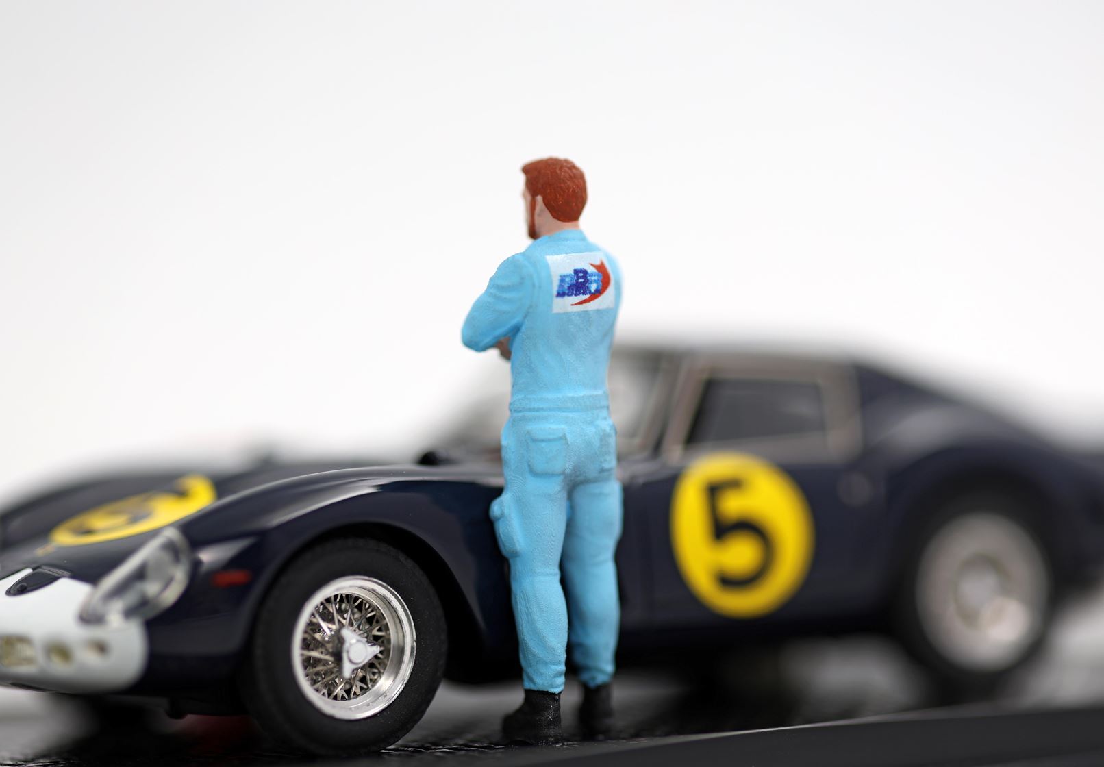 Miniatura di un meccanico in divisa blu accanto a un'auto da corsa nera con il numero 5 giallo, disponibile su Vroomi.