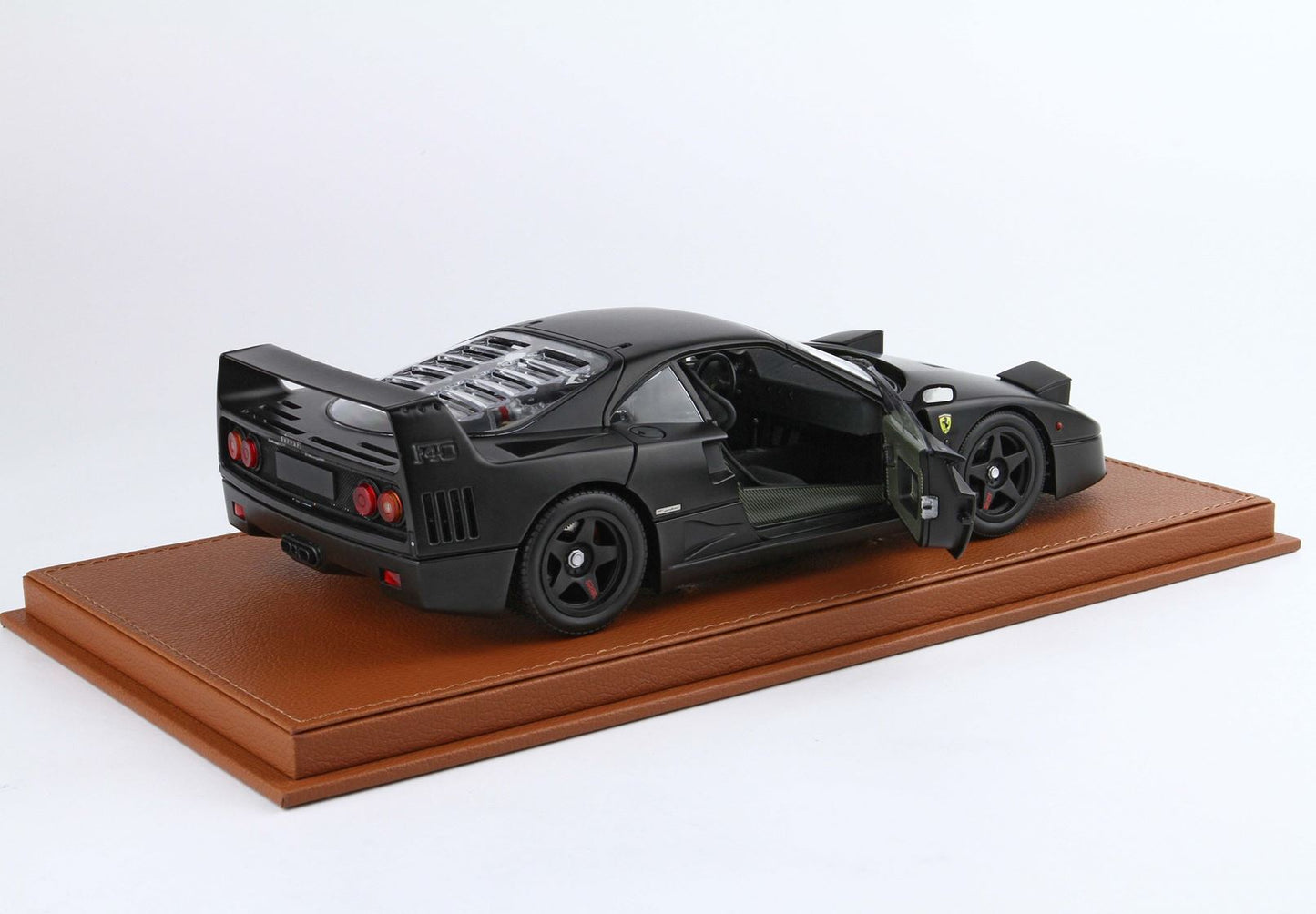 Matte black Ferrari F40 model car with open door on brown leather display base, available on Vroomi