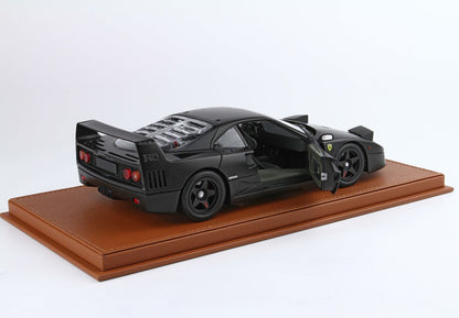 Matte black Ferrari F40 model car with open door on brown leather display base, available on Vroomi